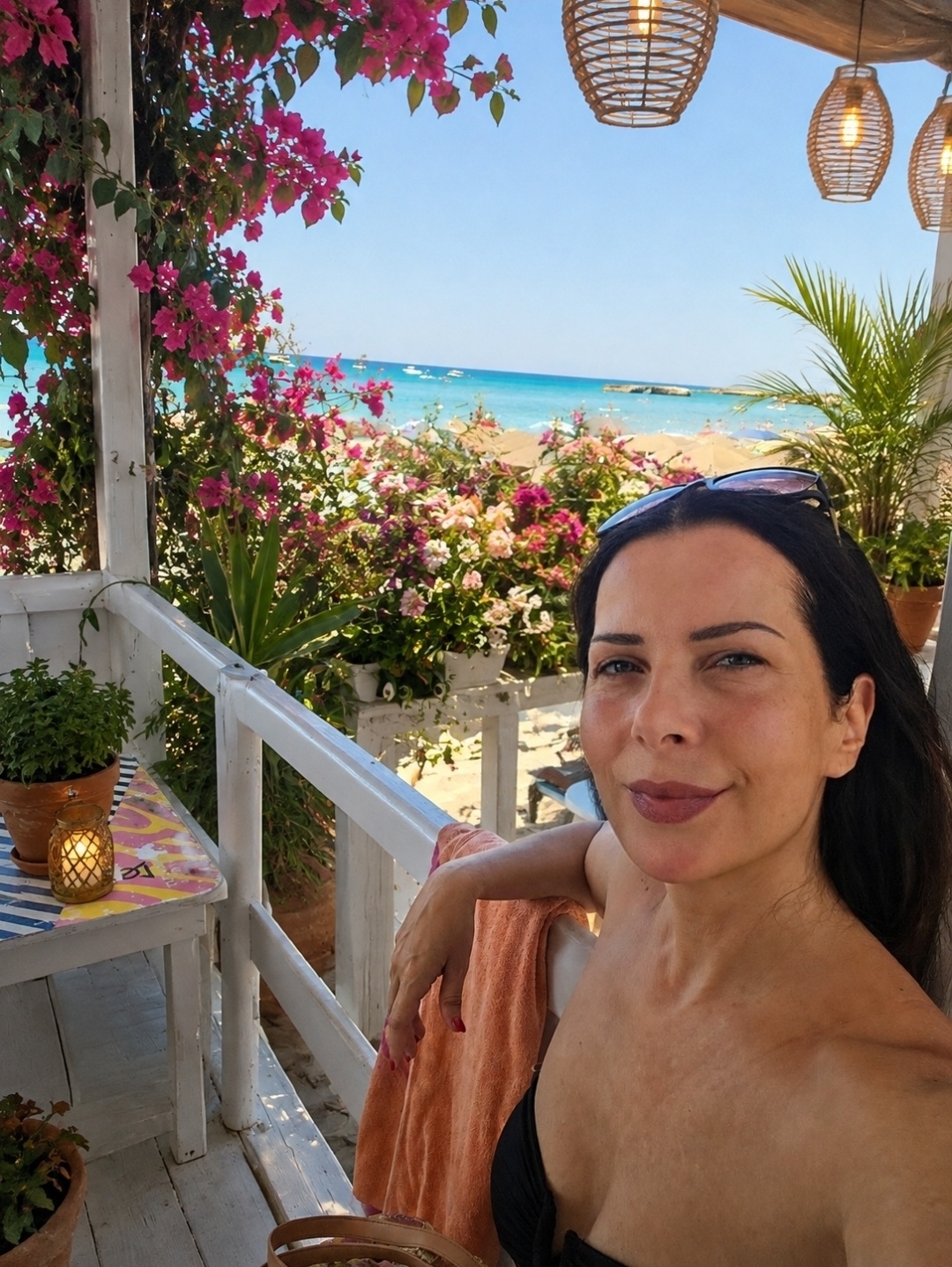 Gabriella Tommasi lächelt auf einer Strandterrasse mit Bougainvilleen und türkisem Meer – Verliebe dich in dein Leben