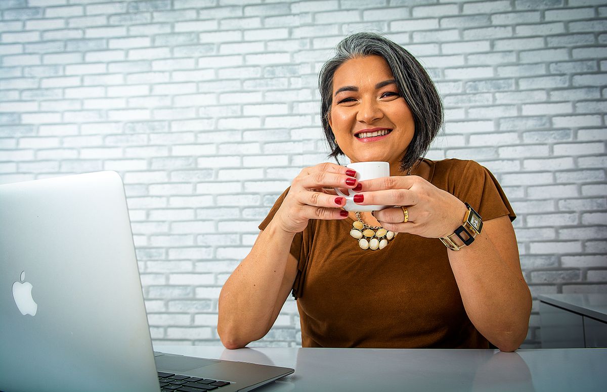 Lächelnde Frau mit grauen Haaren arbeitet mit Kaffee am Laptop – Karriere ab 40